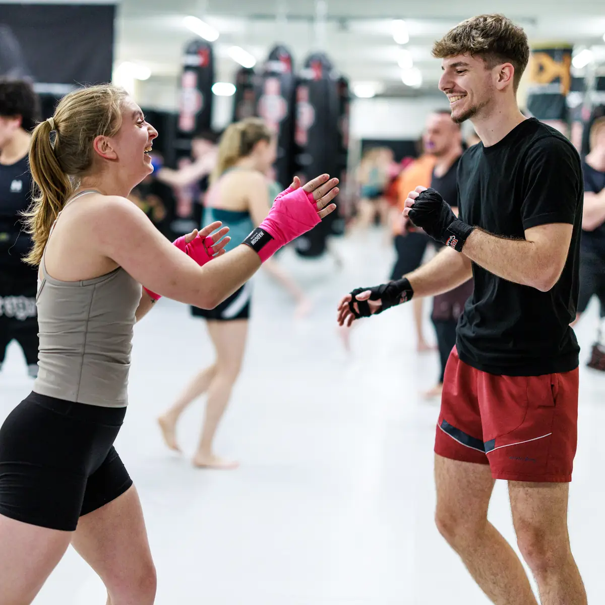 Lachende Teilnehmer einer vollen Kickbox-Einsteigerklasse beim Partnertraining